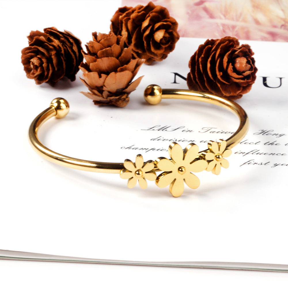 Gold colored hard bracelet with three small flowers of different sizes