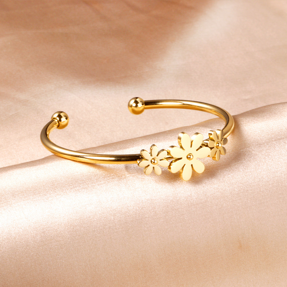 Gold colored hard bracelet with three small flowers of different sizes